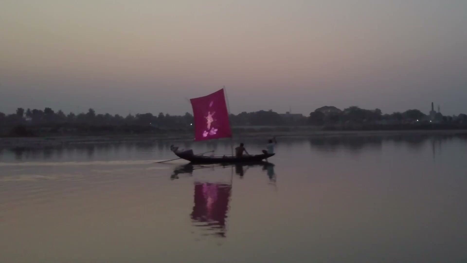 Film still of a boat with a red sail crossing a calm river at dusk