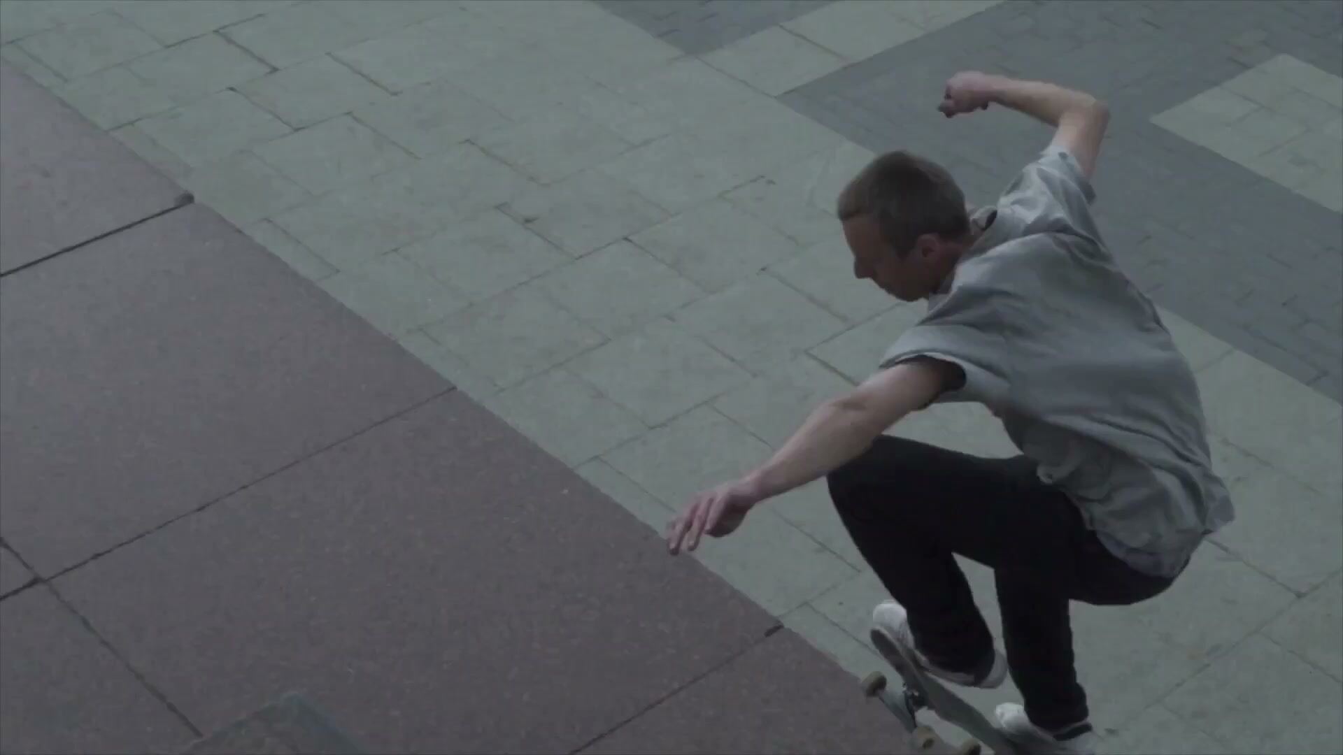 Film still of a skateboarder mid-trick on a paved city plaza