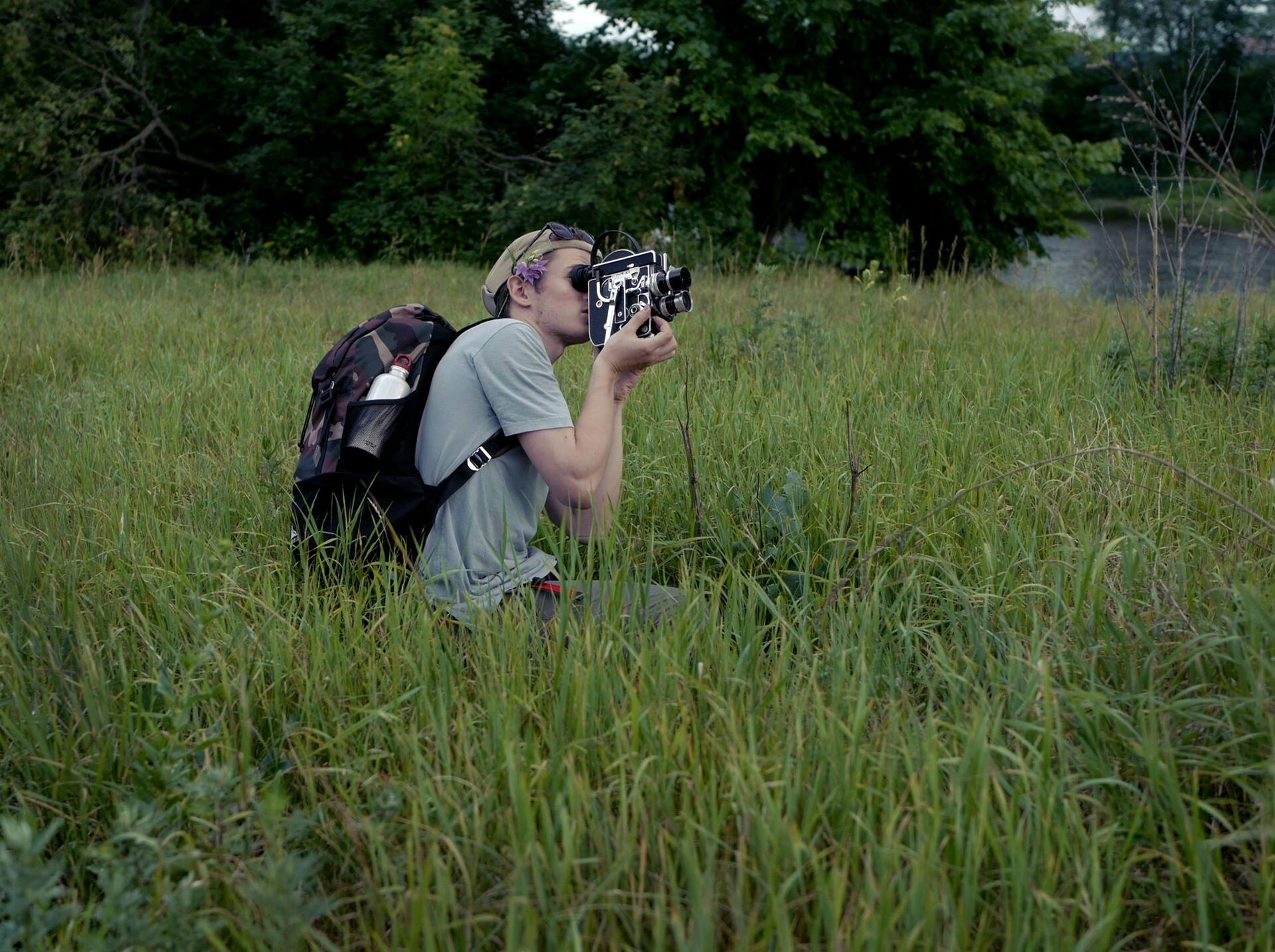 Cinematographer crouching in tall grass, filming with a handheld cinema camera