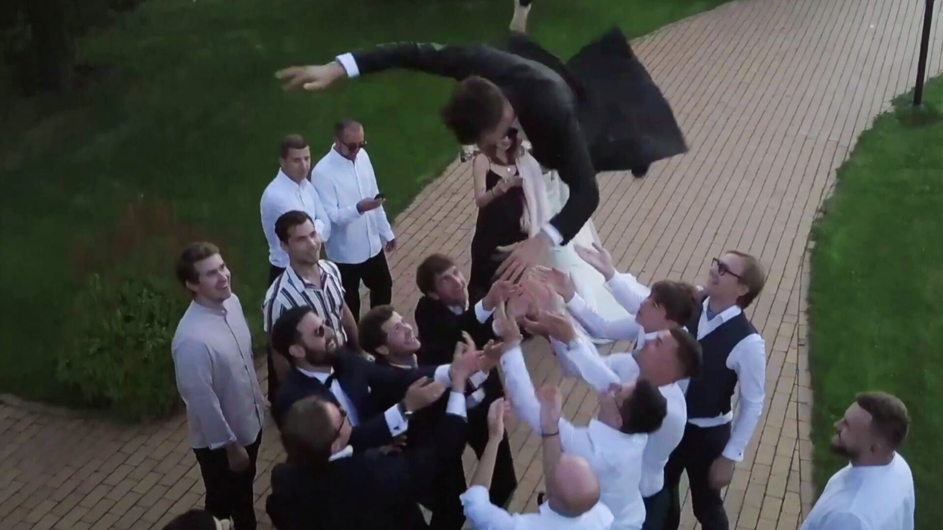 Groomsmen tossing the groom into the air on a brick path, seen from above