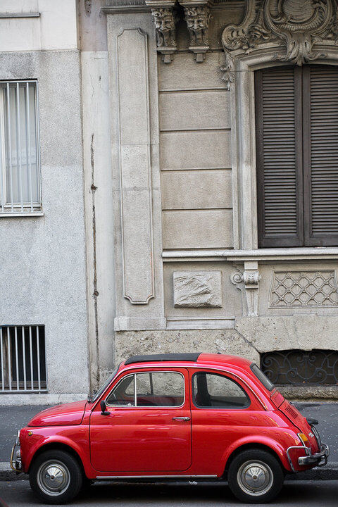 Red vintage Fiat 500 parked beside an old stone building
