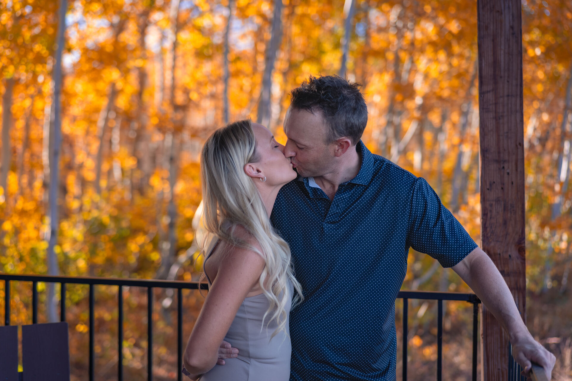 Couple kissing on a balcony surrounded by golden autumn aspens in Park City, Utah