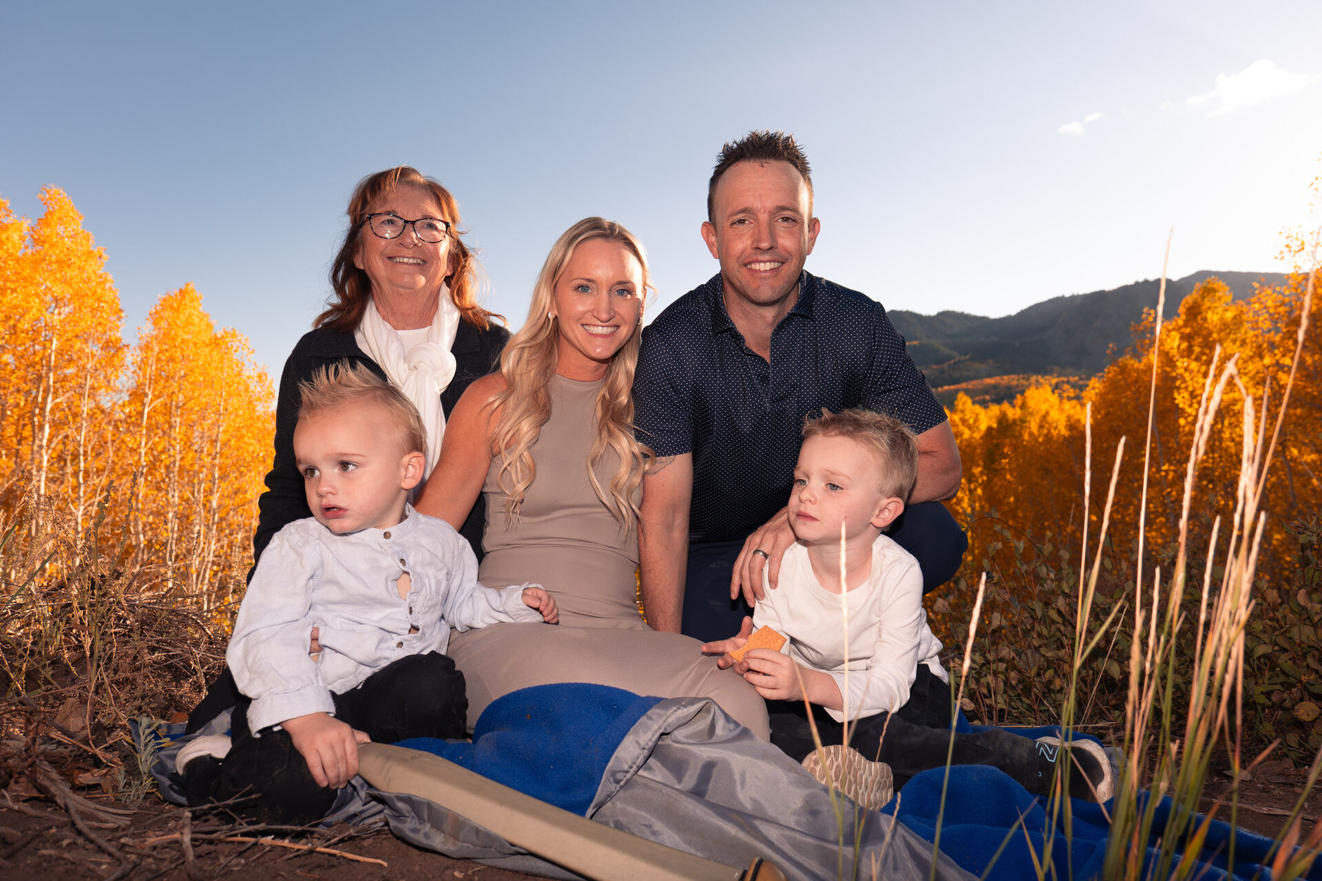 Family of five sitting together among golden aspens at sunset in Park City, Utah