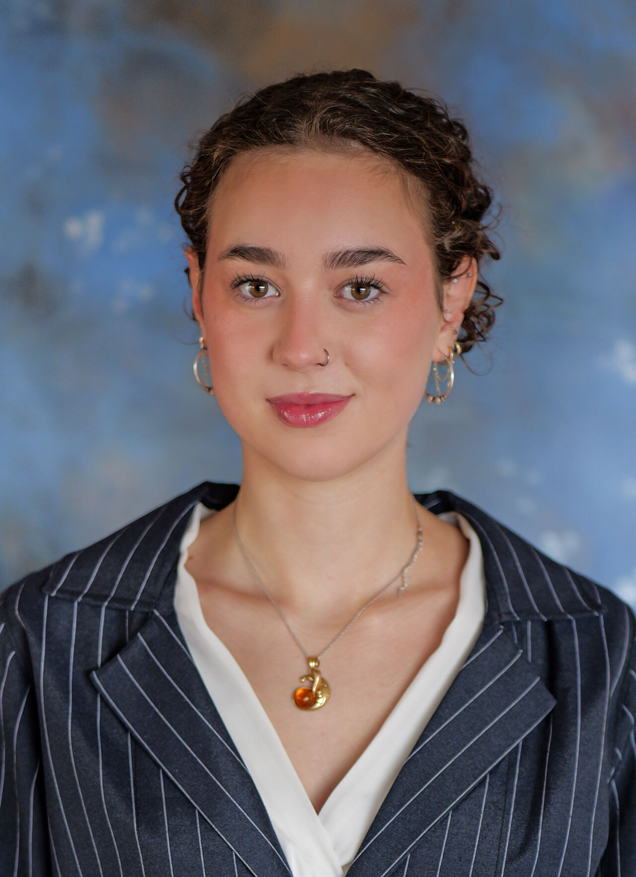Studio headshot of a young woman in a pinstripe blazer against a painted blue backdrop
