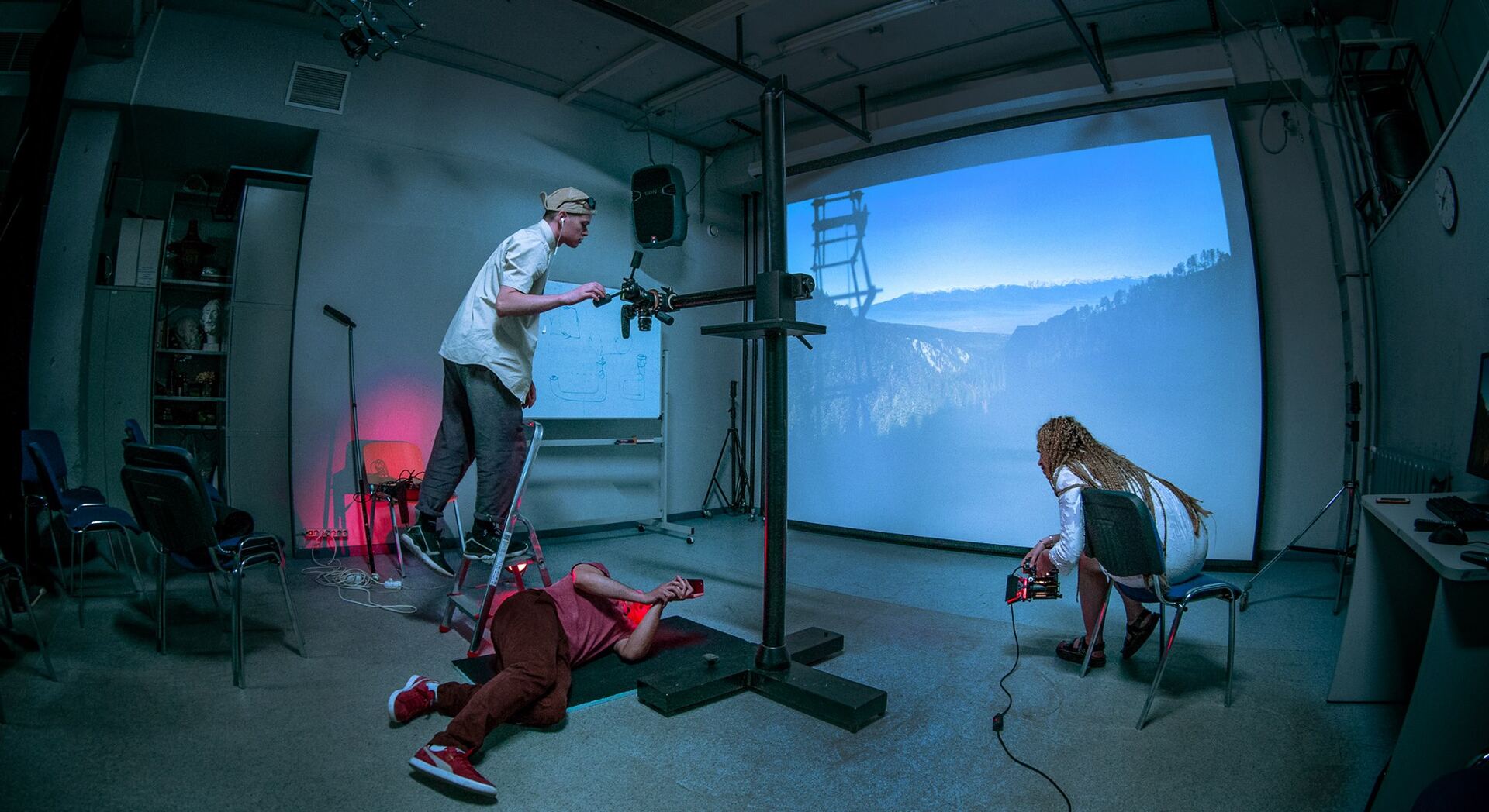 Camera operator filming performers in a studio in front of a large projected mountain backdrop